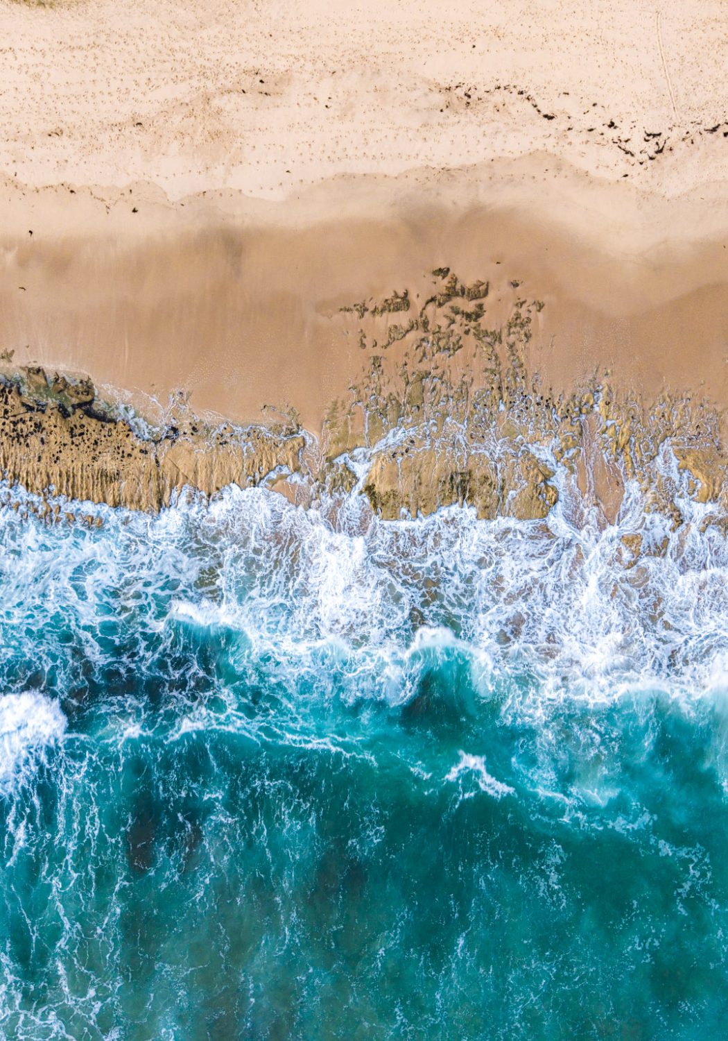 Aerial photograph of turquoise waves meeting the sand at Thirteenth Beach