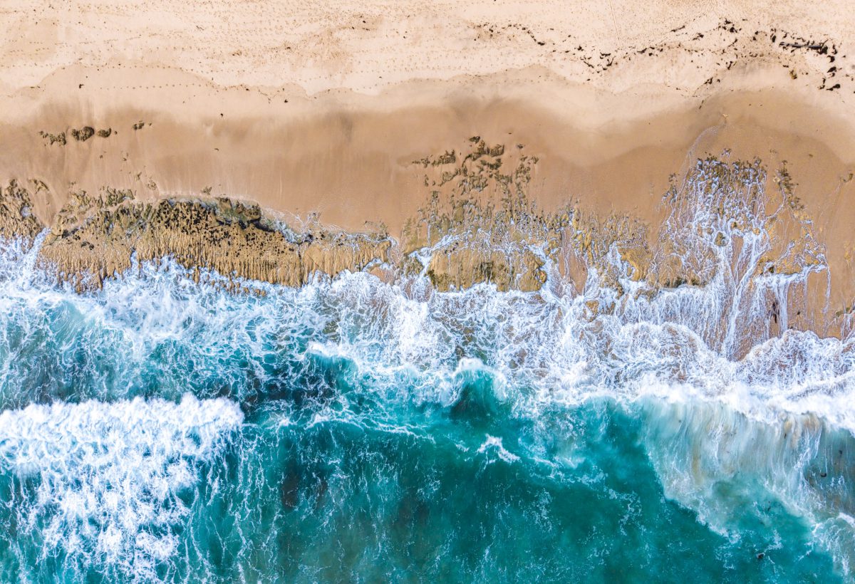 Aerial photograph of turquoise waves meeting the sand at Thirteenth Beach