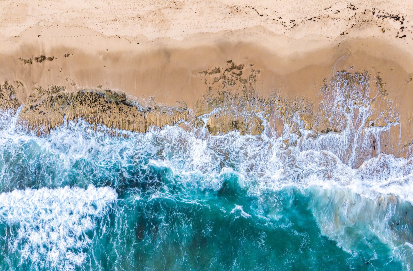 Aerial photograph of turquoise waves meeting the sand at Thirteenth Beach